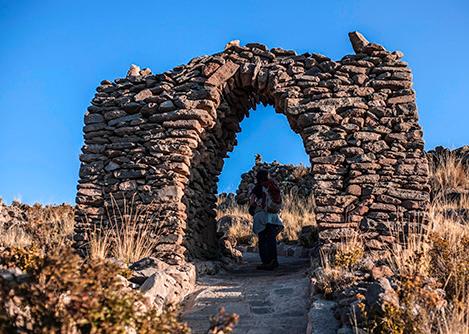 A visitor walking under an archway built from stones on Amantaní Island in Lake Titicaca.