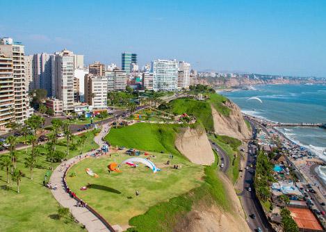 Paragliders at the Costa Verde, green cliffs lined with modern high rises overlooking a highway.