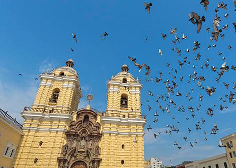 Pigeons flying in front of the yellow Basilica and Convent of San Francisco in Lima.