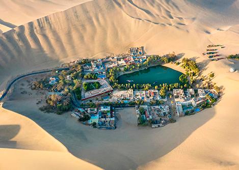 Aerial view of the Huacachina Oasis surrounded by palm trees and various buildings.