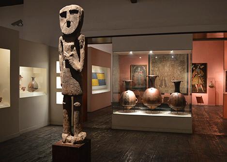 A statue on display at the Larco Museum, with various other exhibits visible in the background.