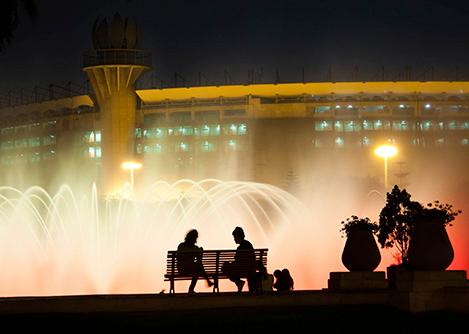 Two visitors sitting on a bench in front of a water fountain at Lima's Magic Water Circuit.