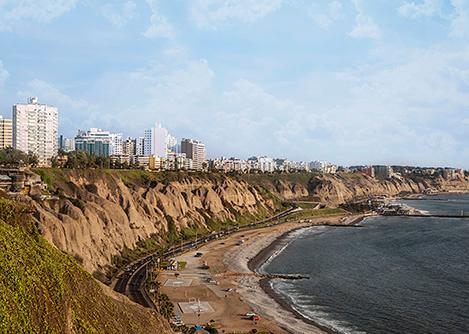 High rise buildings lining the verdant cliffs of the Costa Verde, with a highway and beaches below.