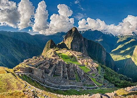 View of Machu Picchu and surrounding mountains, with fluffy white clouds overhead.