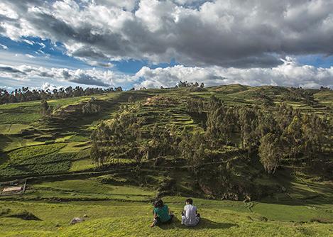 Two people sitting on a hill overlooking trees and agricultural fields in Peru's Sacred Valley.