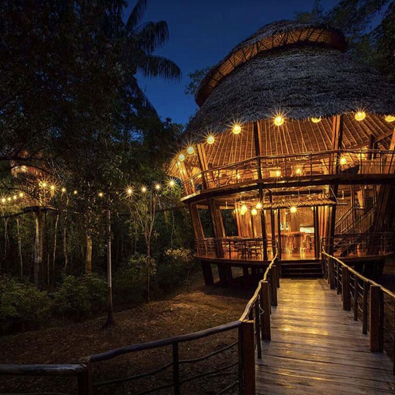 An Amazon Jungle lodge that is being pictured in the evening as the sky is dark. The jungle lodge is built to be mostly outdoors