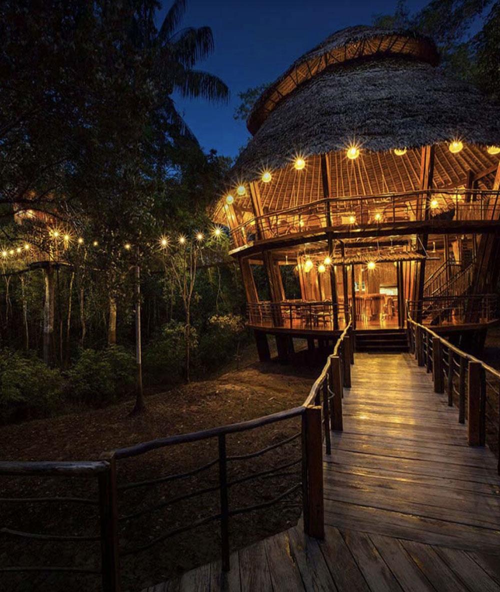 An Amazon Jungle lodge that is being pictured in the evening as the sky is dark. The jungle lodge is built to be mostly outdoors