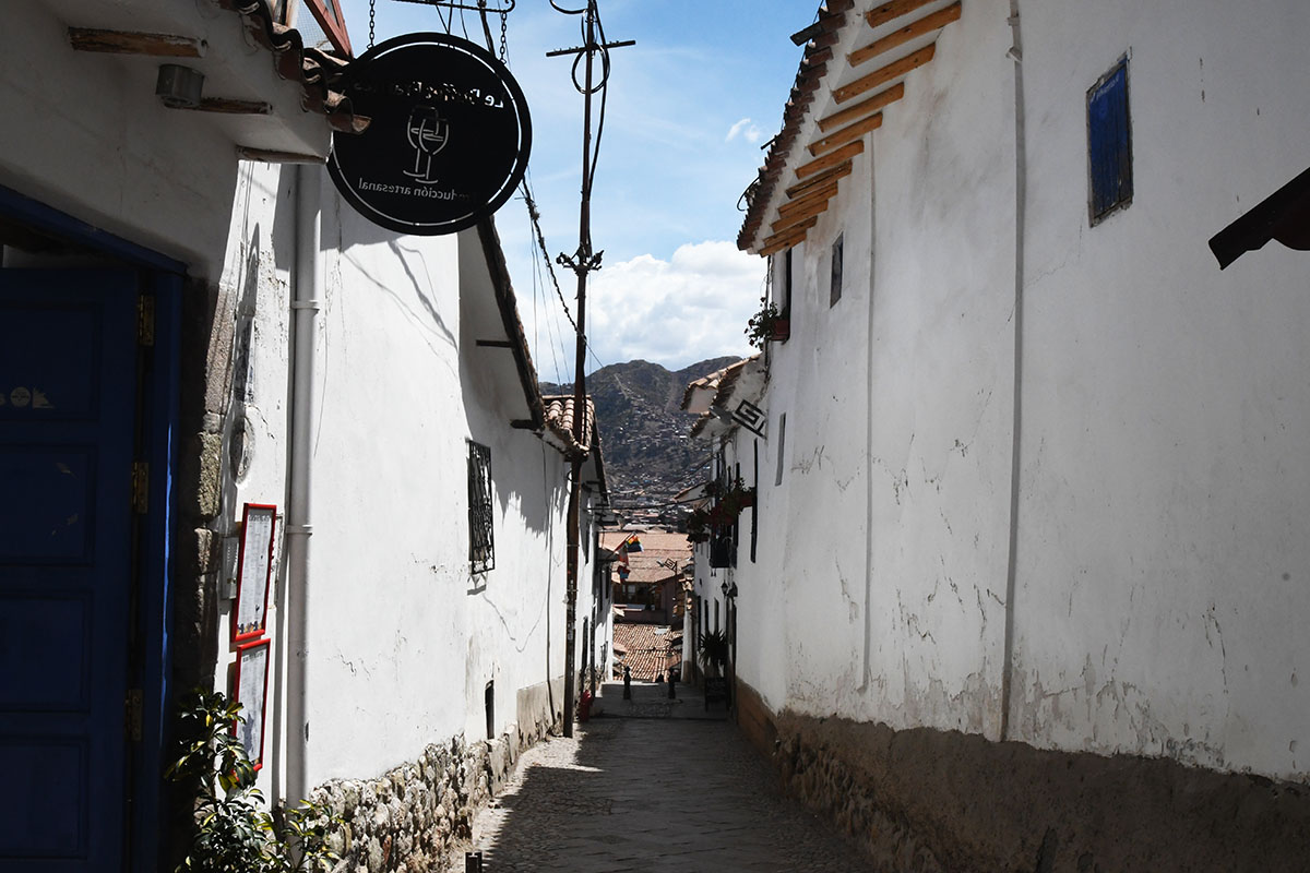 A romantic, narrow cobblestoned street with white-walled buildings in Cusco's San Blas neighborhood.