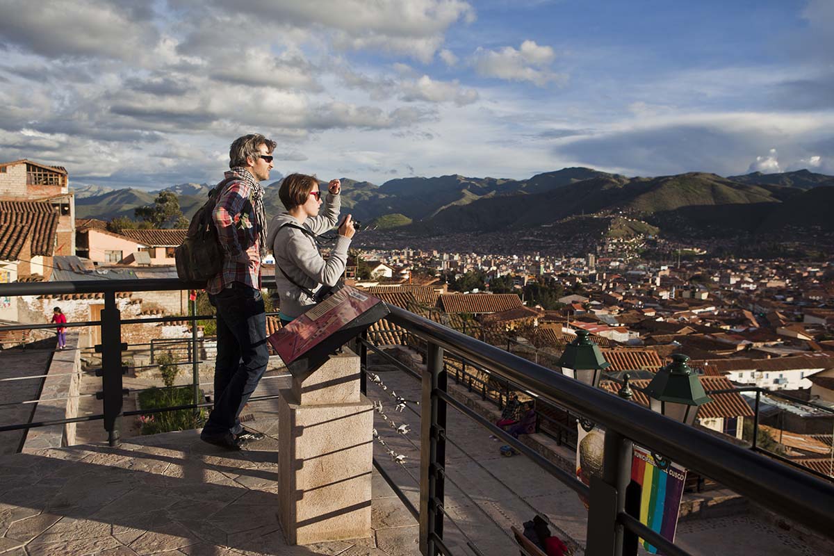 A honeymooning couple looks over the city of Cusco with green mountain in the background.