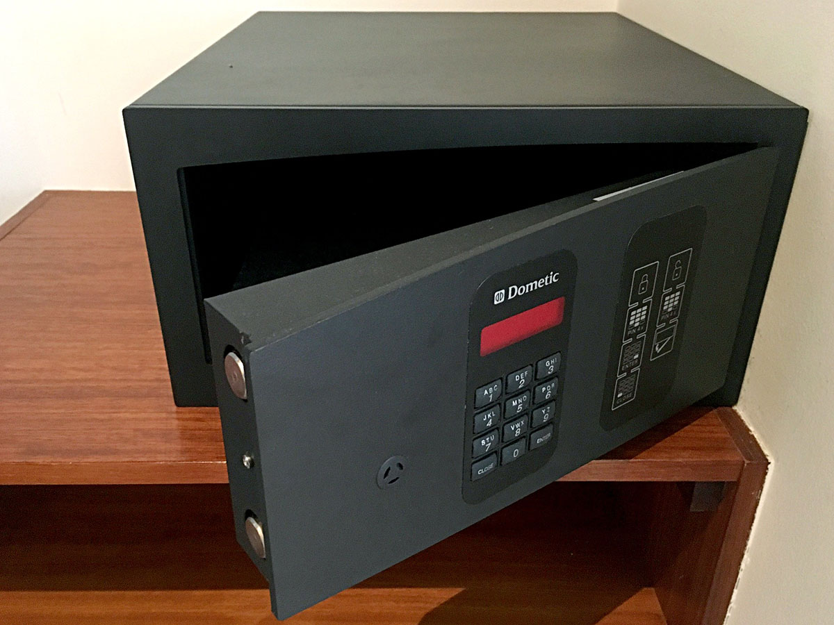 A black hotel safe with its door open and a keypad lock sits on a wooden night stand.