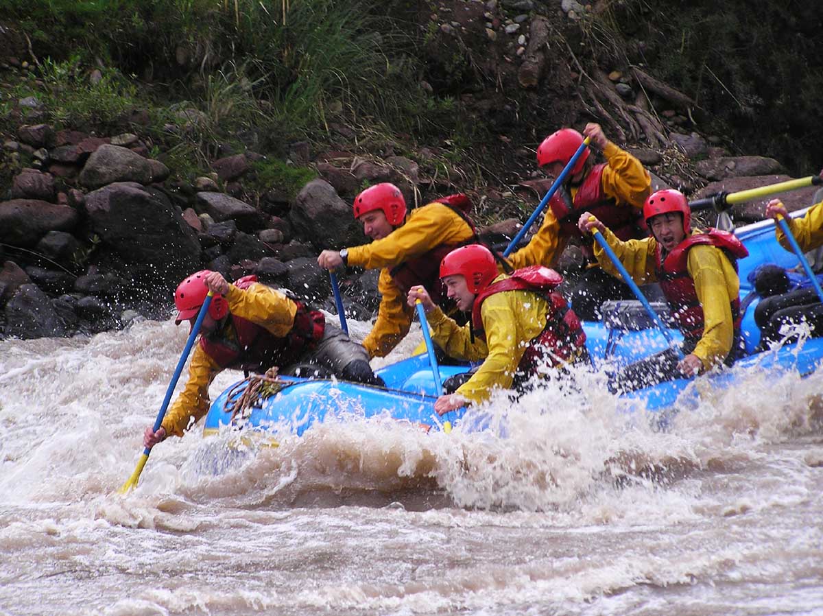 Five people in yellow shirts and red helmets raft down a river.