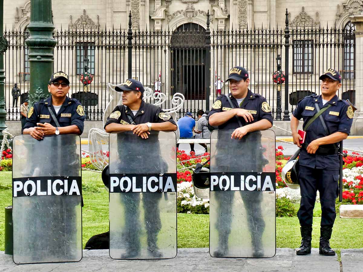 Four Peruvian police officers standing with shields in front of the Presidential Palace.