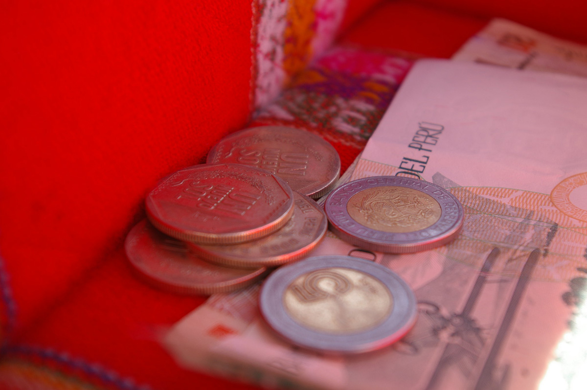 Peruvian coins on top of Peruvian bills inside of a box lined with red woven Andean textile.