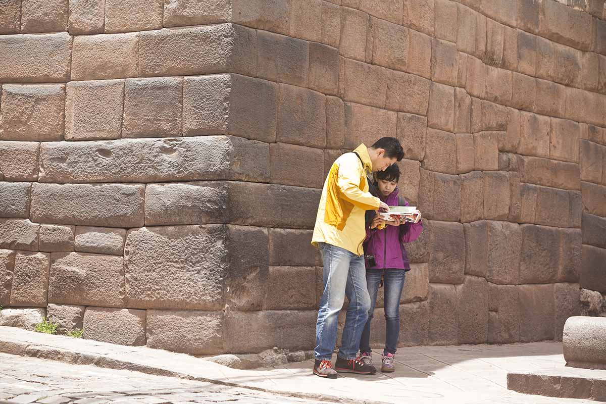 A man and woman stand at the corner of a building in Cusco while they look at a map.